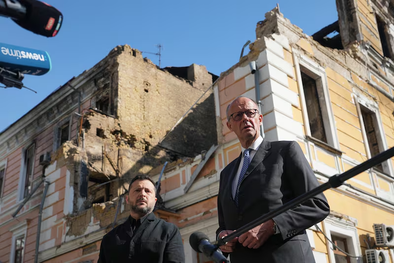 Ukraine's President Volodymyr Zelenskyy, centre, and German Chancellor Friedrich Merz speak to media with National Academy of science building damaged after a Russian drone strike, on the background, Kyiv, Ukraine, Sunday, Oct. 4, 2026. (AP Photo/Evgeniy Maloletka)